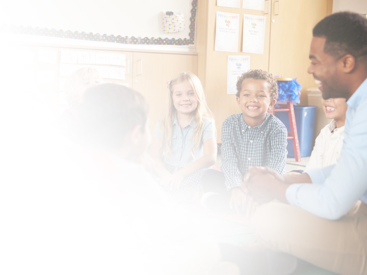 Students and teacher sitting on the floor smiling together.